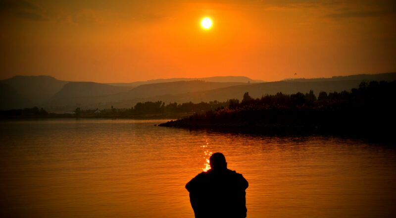 Man thinking by a lake at sunset.