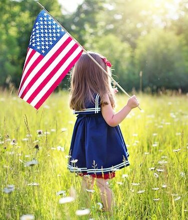 Little girl holding an American flag in a sunny field of flowers on July 4
