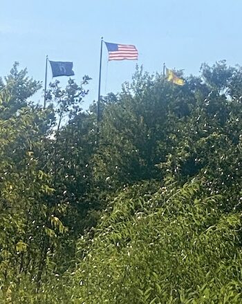 American flag flying high between two smaller flags on a hill.